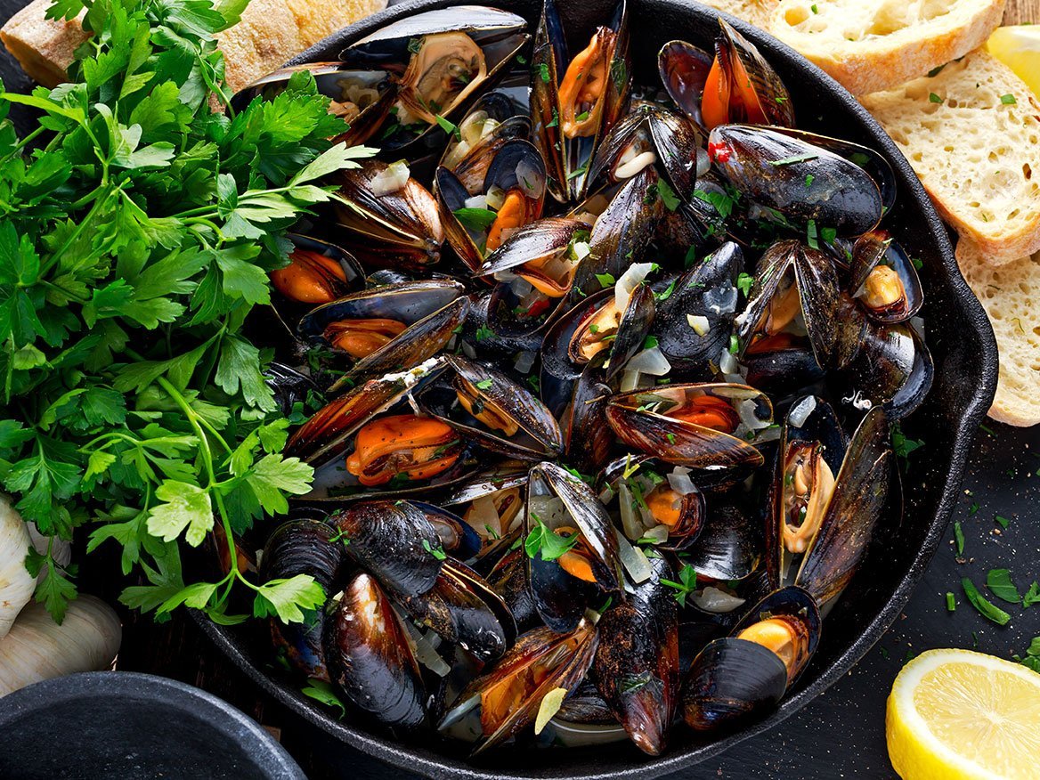 Boiled Mussels In Iron Pan Cooking Dish. With Herbs, Butter, Lime, Parsley, Garlic And Fresh Bread.