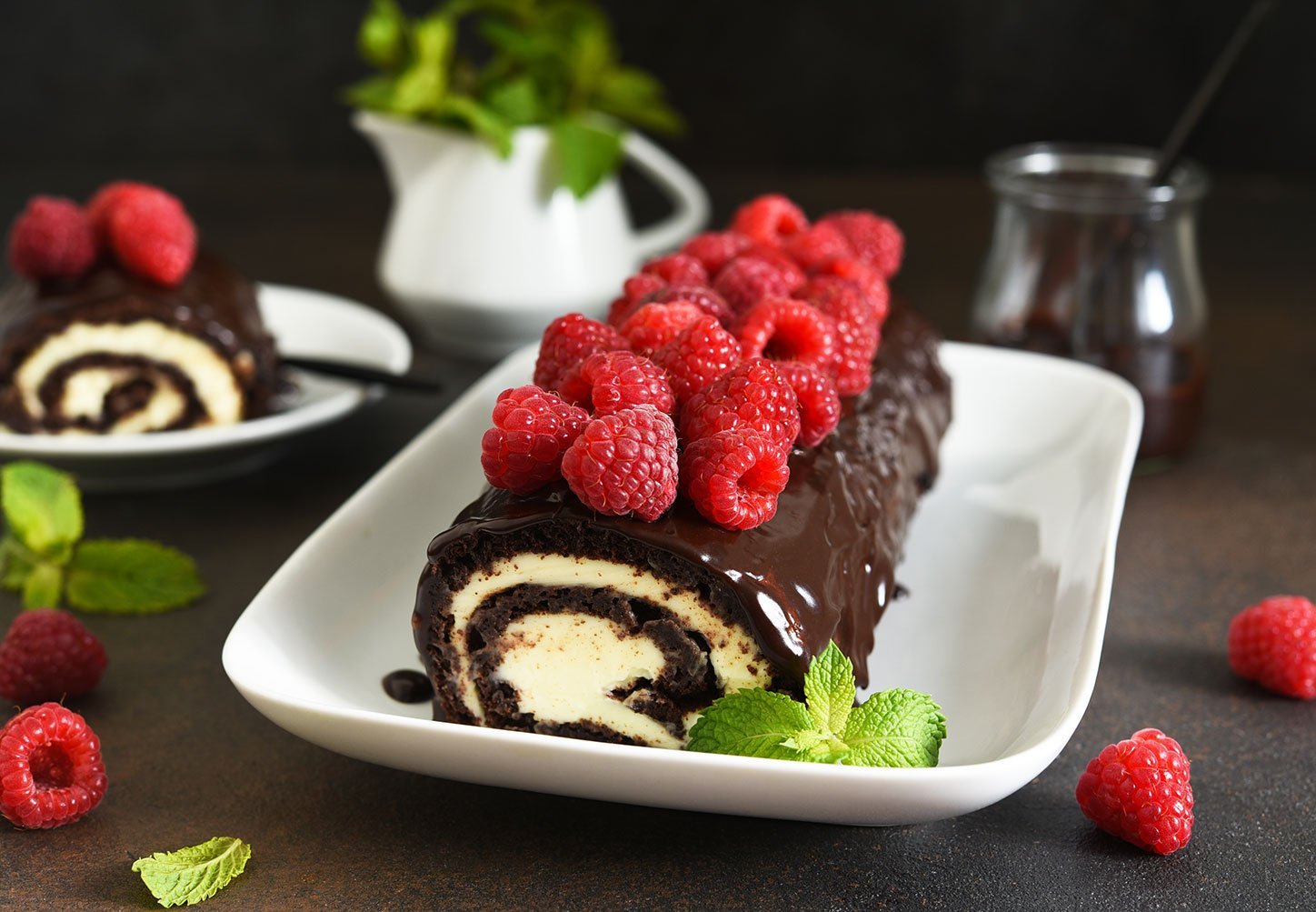 Chocolate Roll With Cream Cheese And Raspberries, With A Cup Of Coffee On A Dark Background.