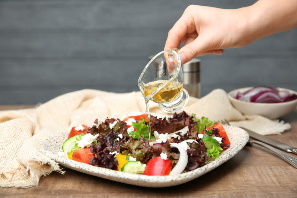 Woman Adding Tasty Apple Vinegar To Salad With Vegetables On Table