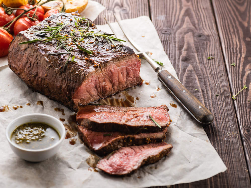 Sliced Roast Beef On White Paper On Wooden Table With Grilled Vegetables.