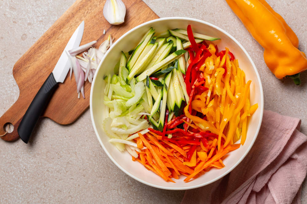 Cutting Fresh Raw , Vegetables, Onion, Julienne Carrot, Bell Peppers, Zucchini, Celery. Knife, Wooden Board. Top View.