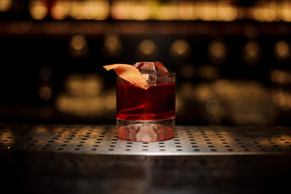 Glass Of A Delicious Boulevardier Cocktail With Orange Zest On The Steel Wooden Bar Counter