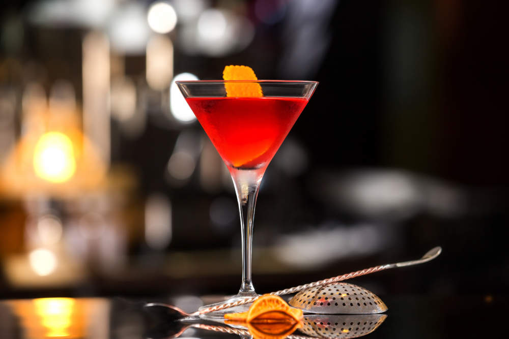 Closeup Glass Of Manhattan Cocktail Decorated With Orange At Bar Counter Background.