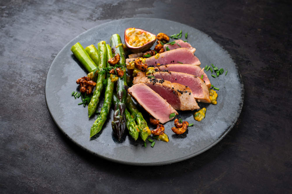Tuna Tataki Steak With Caramelized Green Asparagus, Roasted Cashew And Maracuja Passion Fruit Relish Dip Sauce Served As Close Up On A Design Plate