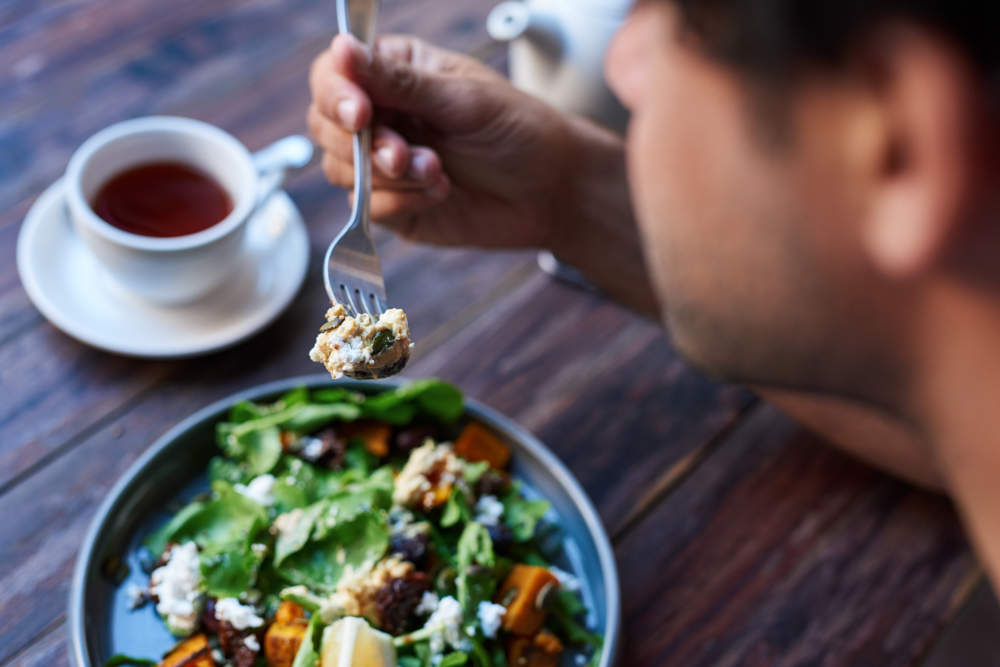 Man Eating Delicious Salad While Sitting At A Bistro Table
