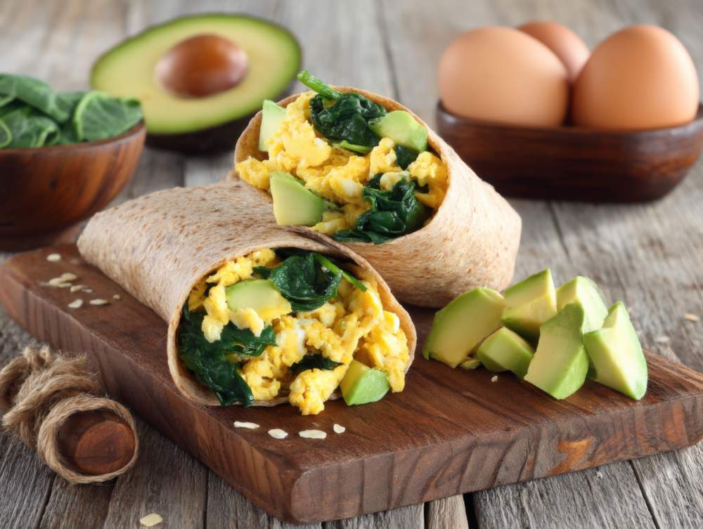 Close Up Of Breakfast Burrito With Eggs Spinach And Avocado On Wooden Board Healthy Eating Concept